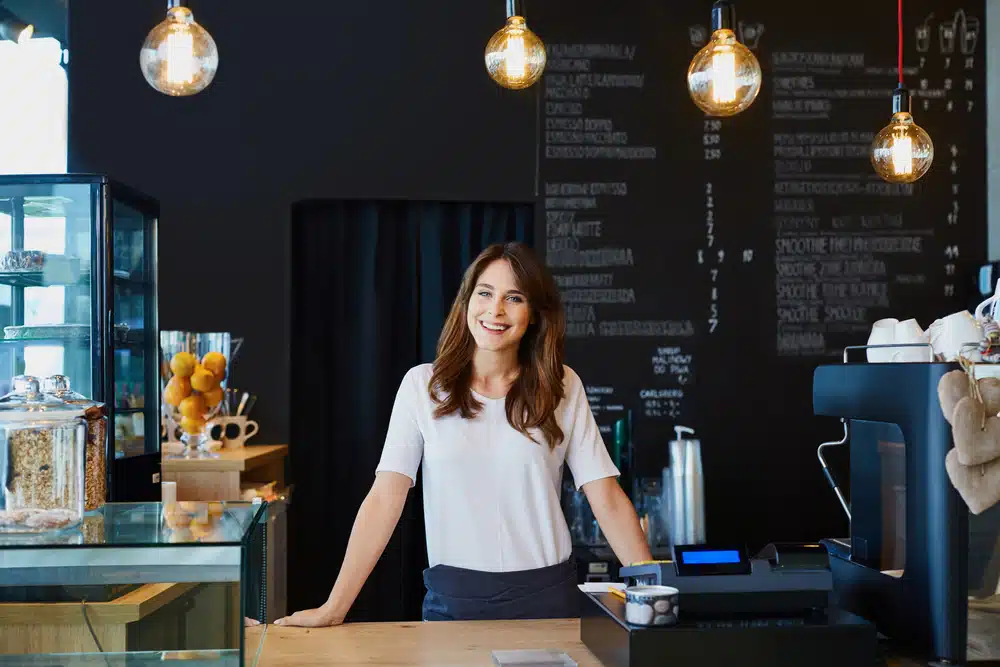 Friendly young woman standing behind the counter of a modern cafe