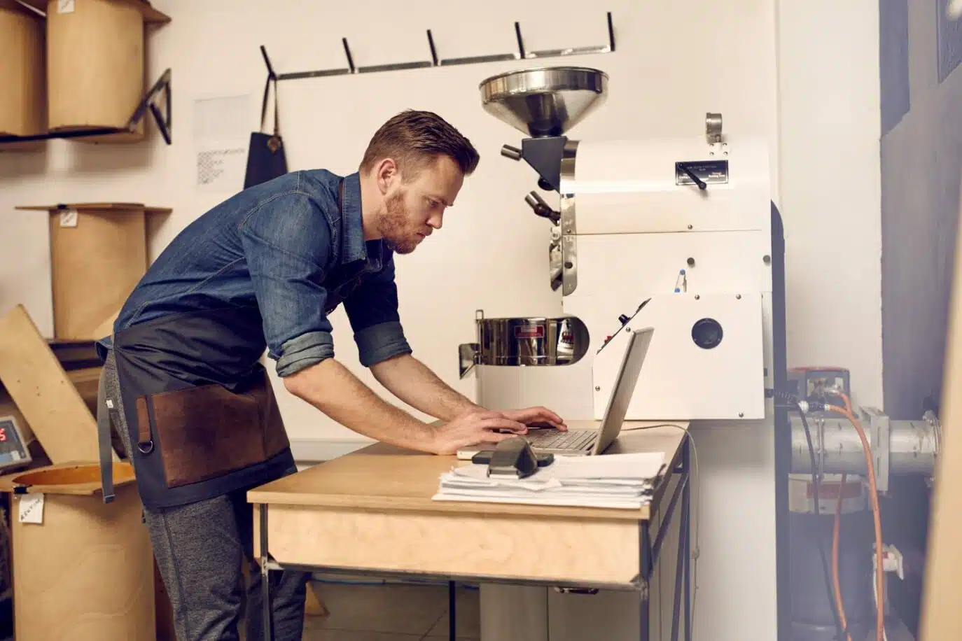 Male small business owner working on laptop beside coffee roasting machine
