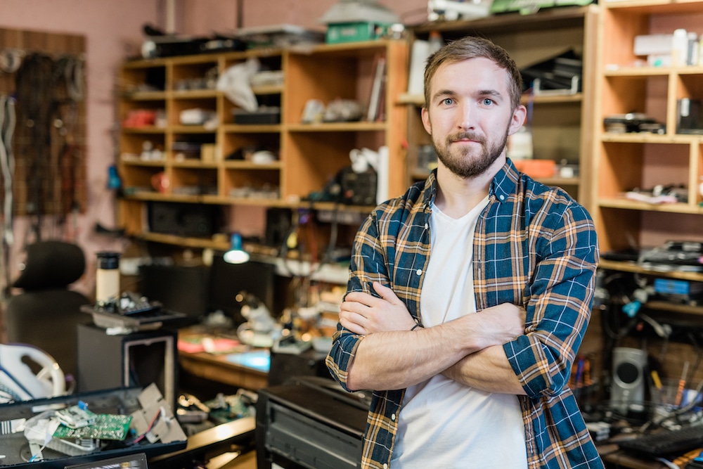 Confident young man standing with arms crossed in an electronics repair workshop