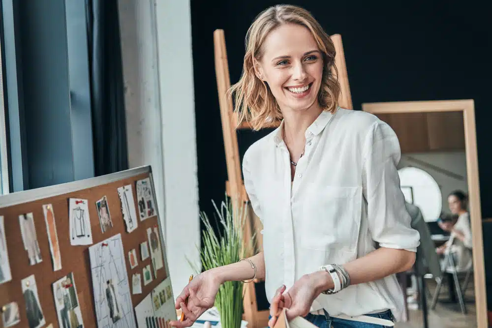 Fashion designer smiling beside mood board in creative studio