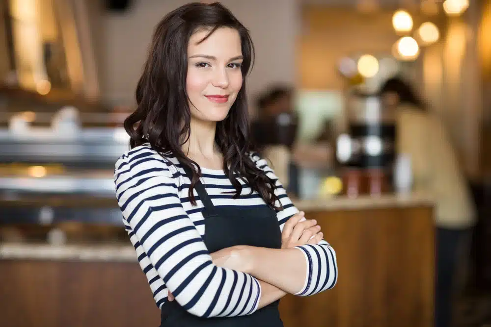 Confident young female cafe owner standing with arms crossed