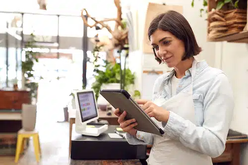 Woman in apron using a digital tablet at her shop’s point-of-sale counter