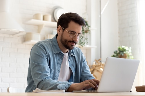 Smiling man in glasses working on a laptop in a bright home office
