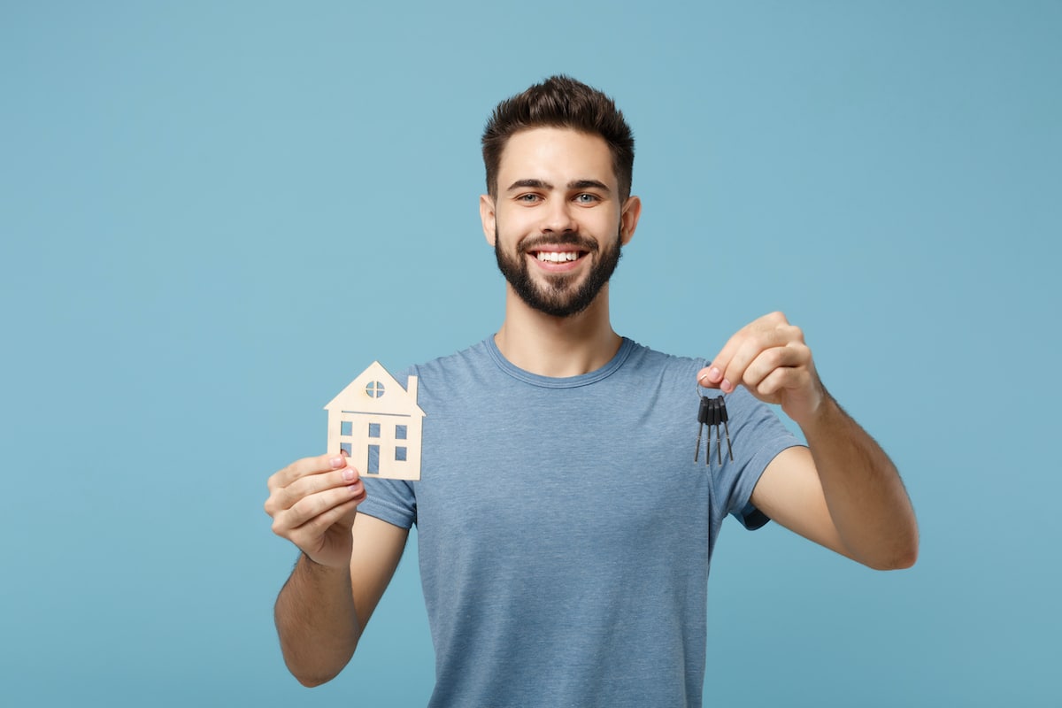Smiling man holding house model and keys against blue background