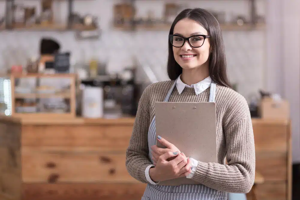 Smiling young cafe owner holding a clipboard inside her coffee shop