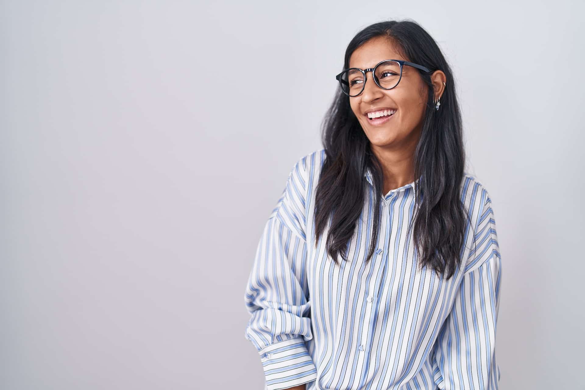 Smiling young woman in striped shirt and glasses standing against a plain background